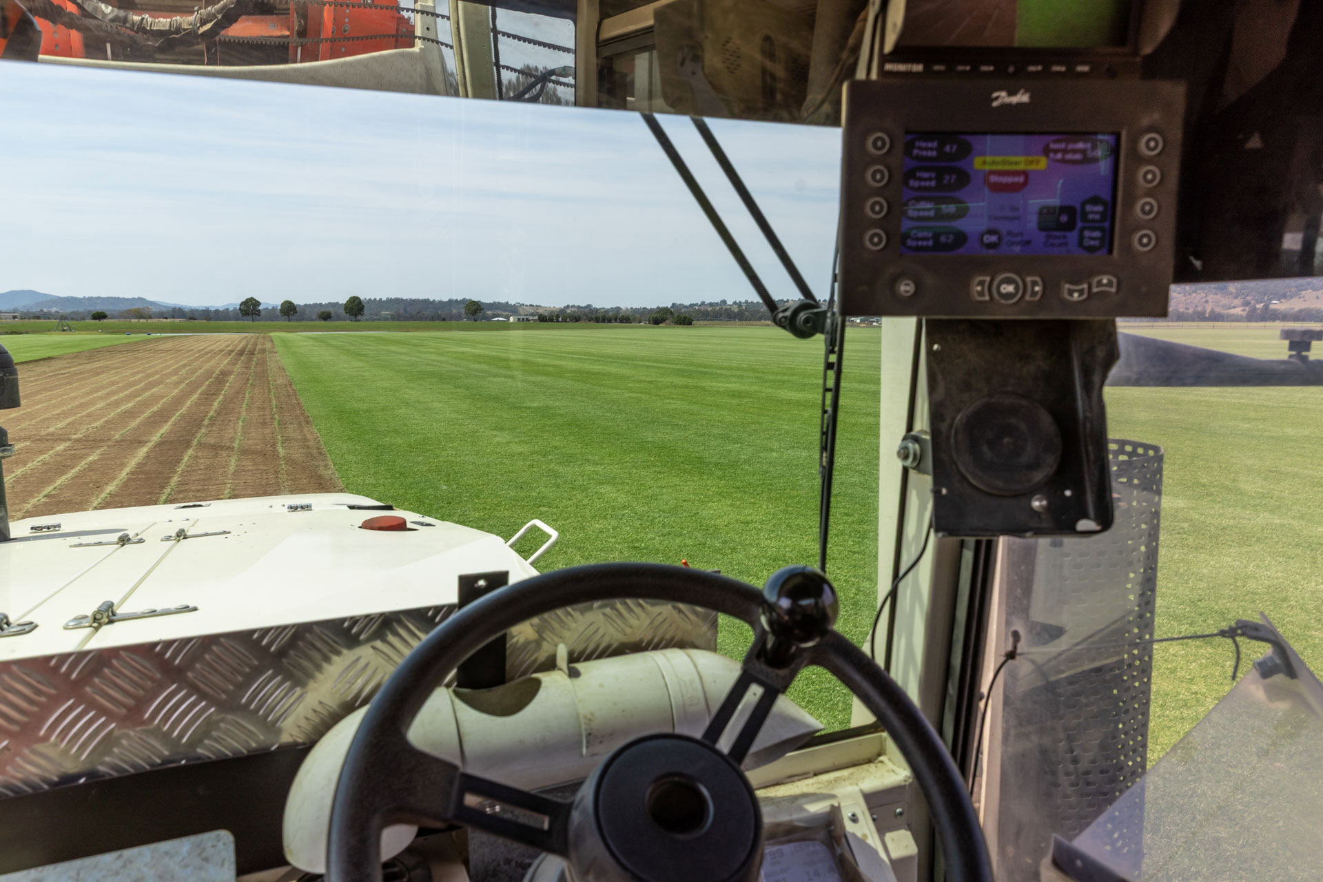 A view from inside the cabin of a tractor or harvester, showing the steering wheel and a digital control monitor.